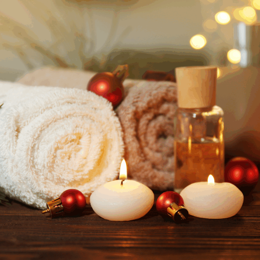 Cedar Meadows Spa & Resort Rolled white and beige towels, a glass bottle, and two lit candles are arranged with red Christmas ornaments on a wooden surface. - Timmins, Ontario
