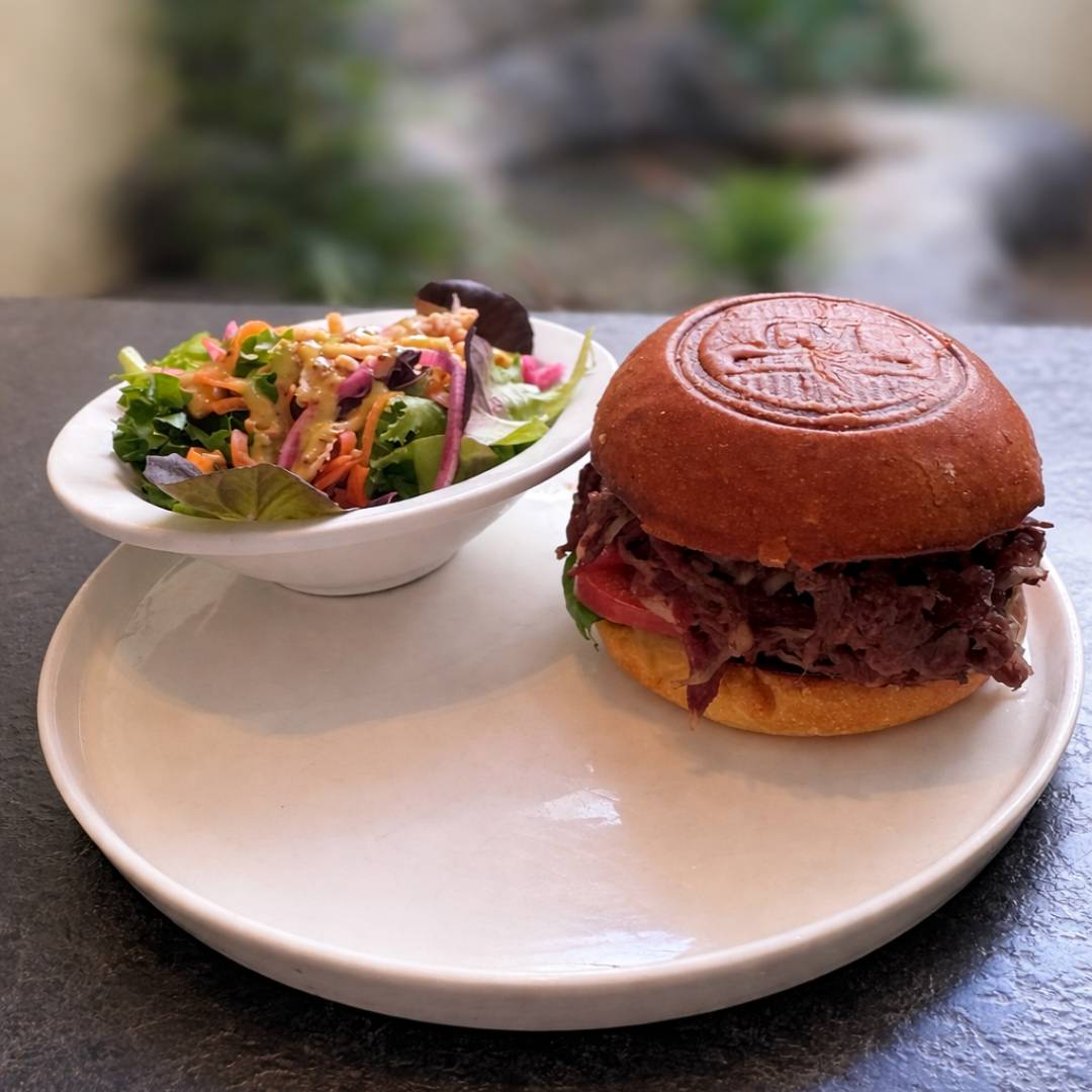 Cedar Meadows Spa & Resort A plate with a beef sandwich on a bun and a small bowl of mixed salad with greens, carrots, and red onions. - Timmins, Ontario