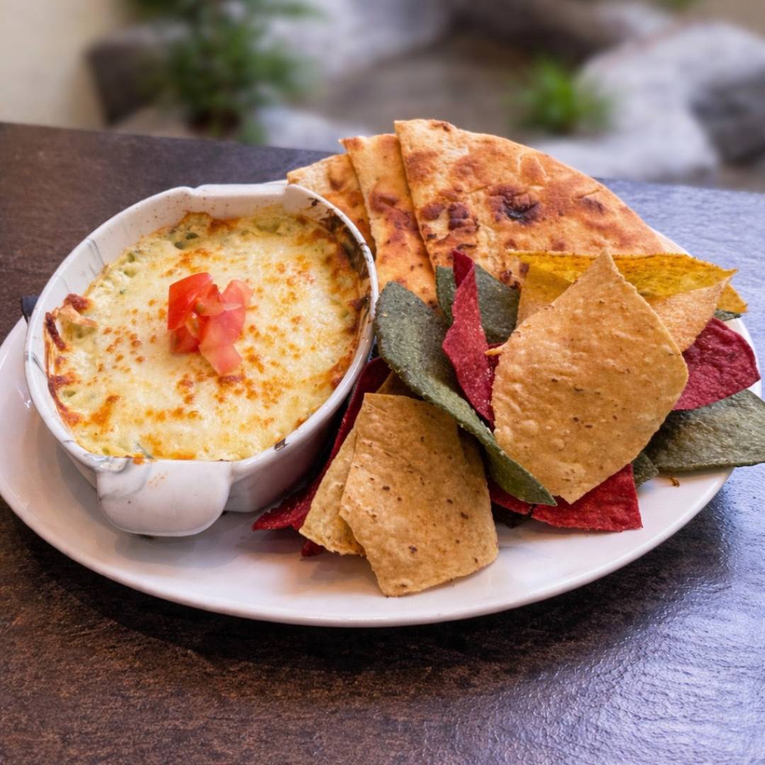 Cedar Meadows Spa & Resort A plate with a baked cheese dip topped with diced tomatoes, served with pita bread slices and colorful tortilla chips. - Timmins, Ontario