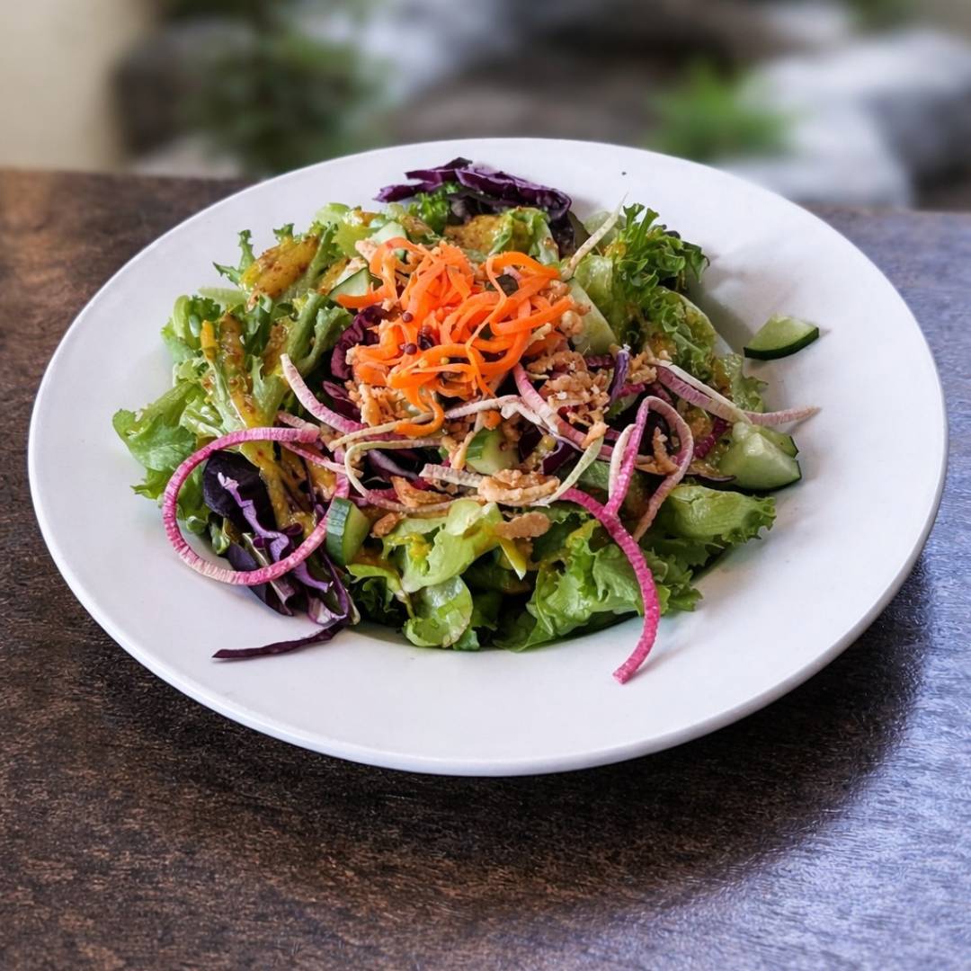Cedar Meadows Spa & Resort A plate of mixed green salad topped with shredded carrots, red onions, purple cabbage, and dressing on a white plate. - Timmins, Ontario