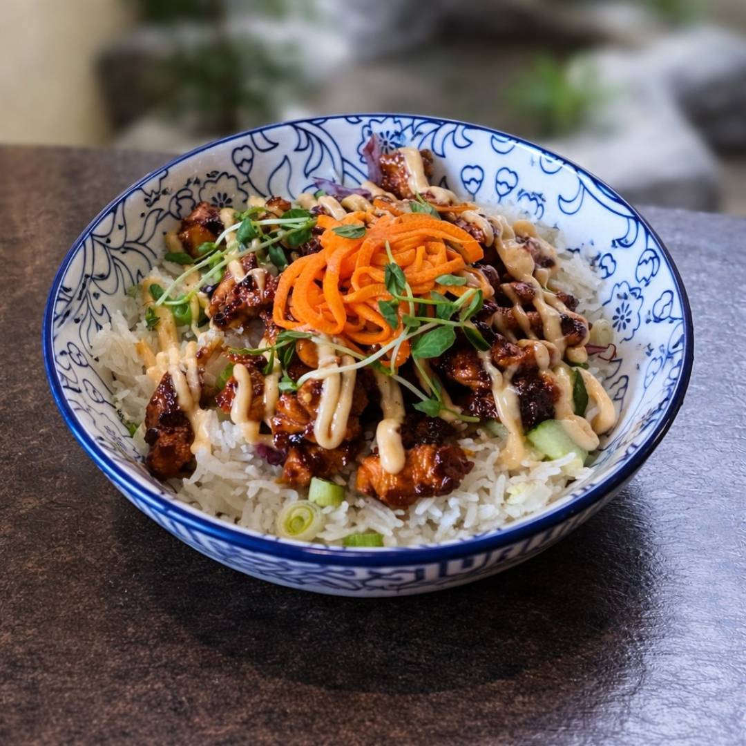 Cedar Meadows Spa & Resort A patterned bowl filled with white rice, grilled chicken, shredded carrots, green onions, cucumber, leafy greens, and a drizzle of creamy sauce. - Timmins, Ontario