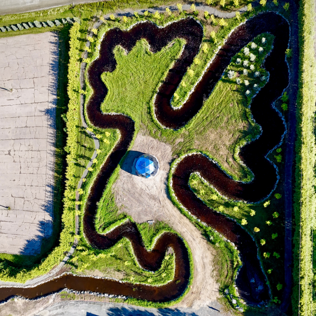 Cedar Meadows Spa & Resort Aerial view of a grass maze with winding paths and a small hexagonal pavilion at the center, bordered by farmland and greenery. - Timmins, Ontario