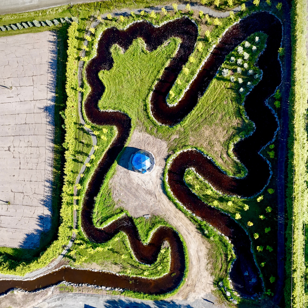 Cedar Meadows Spa & Resort Aerial view of a grass maze with winding paths and a small hexagonal pavilion at the center, bordered by farmland and greenery. - Timmins, Ontario